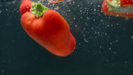 Close-up-several-cut-slices-of-fresh-green-and-red-bell-pepper-thrown-and-floating-in-clear-transparent-water-low-angle-side-view-slow-motion